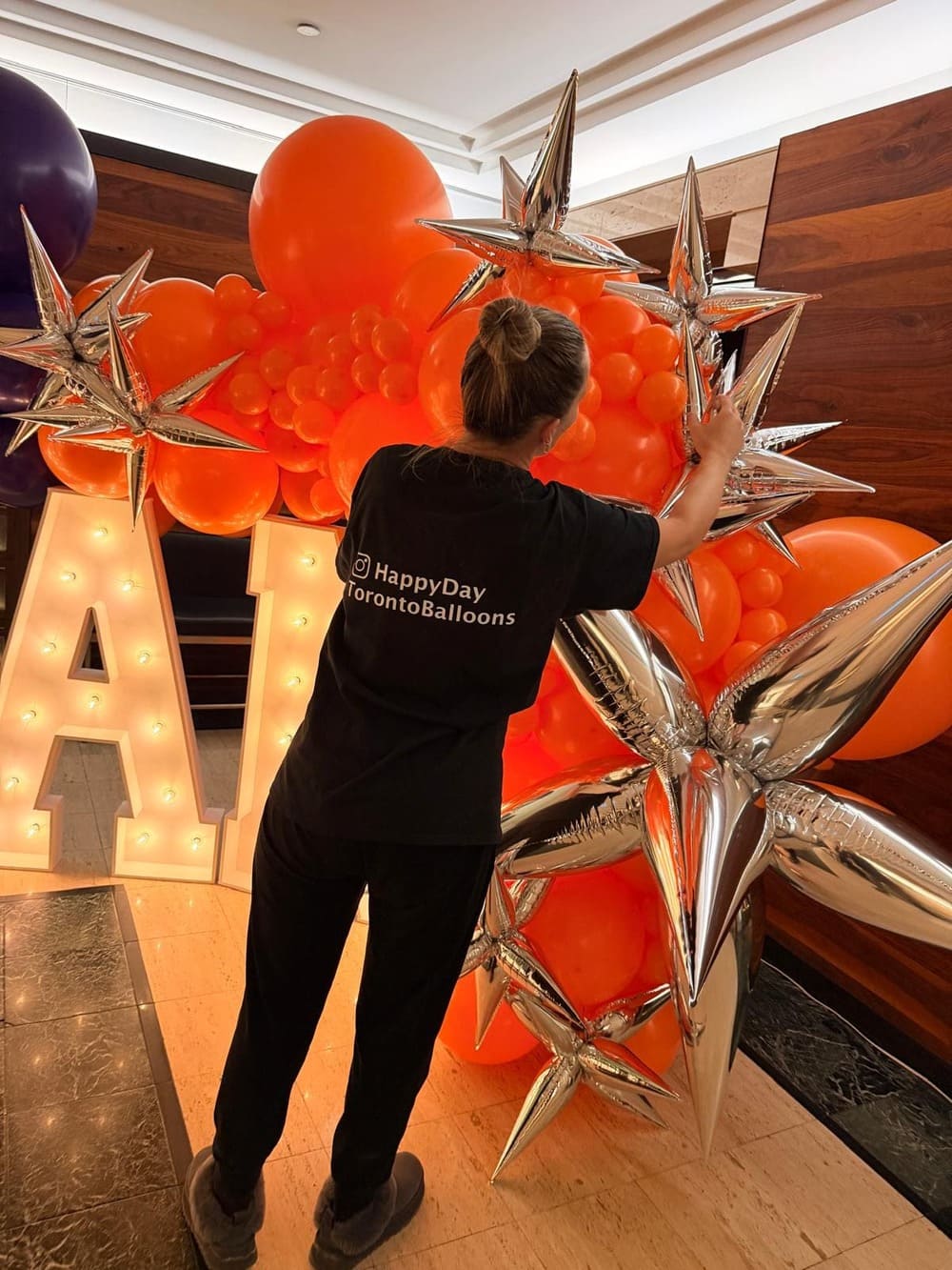Happy Day Toronto decorator building a bright orange balloon installation with metallic stars